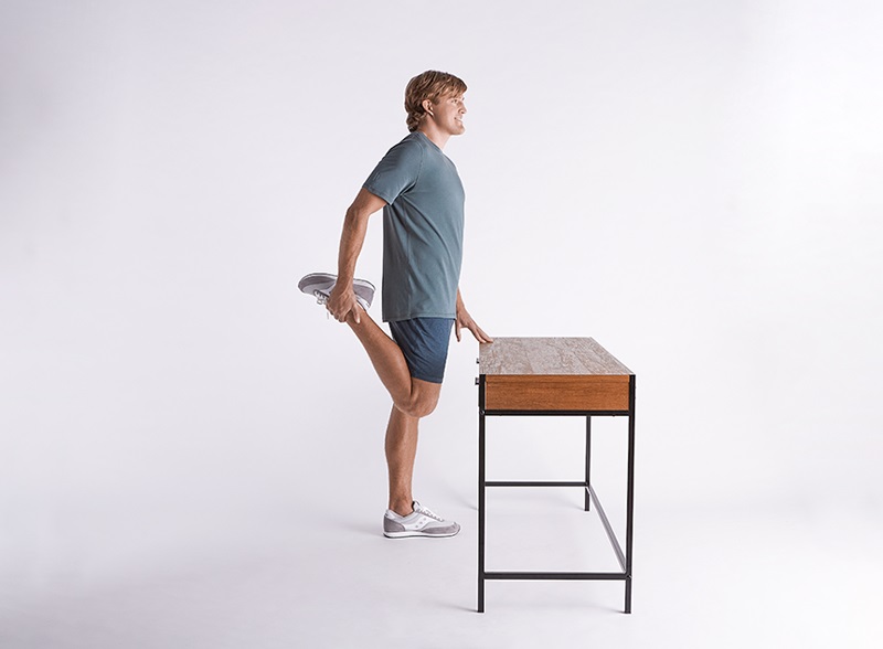Man doing quad stretch while gently leaning on table